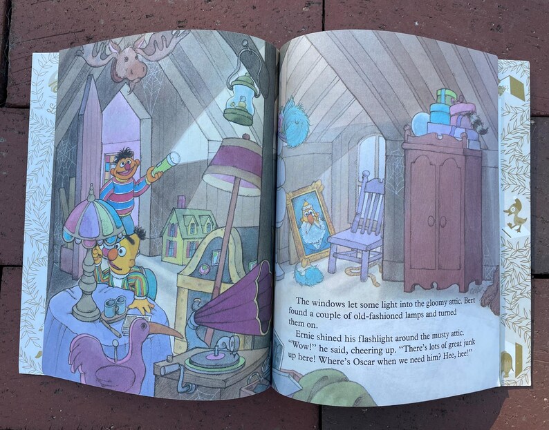 May include: A colorful illustration from a children's book depicts a cluttered attic scene. Two Sesame Street characters, Bert and Ernie, are exploring the attic. The image includes a gramophone, lamps, a framed portrait, and a wardrobe.