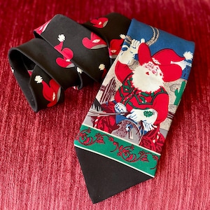 May include: A festive necktie featuring a cowboy Santa Claus design. The tie has a black base with a repeating pattern of red cowboy hats. The main design shows Santa roping a steer, with a green and red border.