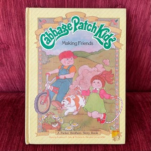 May include: A hardcover Cabbage Patch Kids Making Friends storybook with a light yellow cover. The illustration features a child on a red bicycle, a child jumping rope, a dog, and a turtle. Text includes the title and A Parker Brothers Story Book.