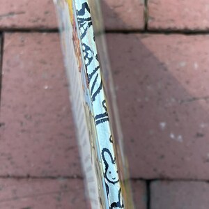 May include: A book's spine with a colorful illustration and black text. The spine has a light blue background with black and white decorative elements. The book is on a brick surface.