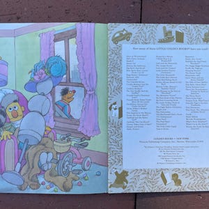 May include: Open pages of a Little Golden Book illustration featuring Sesame Street characters. Bert is in a window, while Ernie sits in a chair with a stuffed animal and toys. The book's title is not visible.