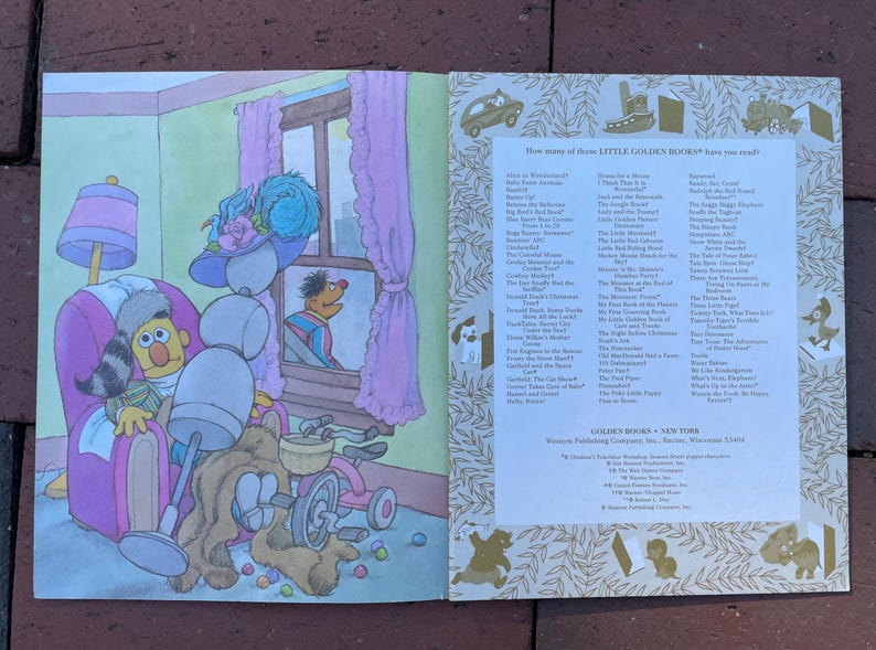 May include: Open pages of a Little Golden Book illustration featuring Sesame Street characters. Bert is in a window, while Ernie sits in a chair with a stuffed animal and toys. The book's title is not visible.