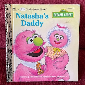 May include: A vintage children's book titled "Natasha's Daddy" from the First Little Golden Book series. The cover features two pink Sesame Street Muppets, with the title in blue text. The book has a gold spine and the Sesame Street logo.