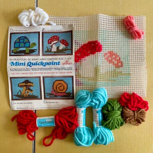 May include: A craft kit for making a 7" x 9" needlepoint project. The kit includes a canvas, yarn in various colors, and instructions. The instructions include a picture of a mushroom, a snail, and a turtle. The kit is labeled "Mini Quickpoint" by Bernat.