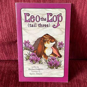 May include: A children's book titled "Leo the Lop (tail three)" with a purple border. The cover illustration features a brown rabbit with long ears, surrounded by purple flowers. The author is Stephen Cosgrove, and the illustrator is Robin James.