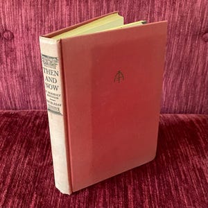 May include: A vintage hardcover book titled "Then and Now" by W. Somerset Maugham. The book has a red cover with the title and author's name printed on the spine. The book is in good condition and appears to be well-preserved.