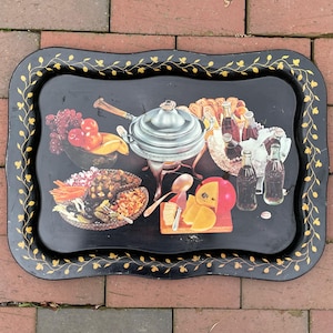 May include: Black serving tray with a gold floral border. The tray features illustrations of food items, including fruit, cheese, and bottles of Coca-Cola. A silver fondue pot is in the center.