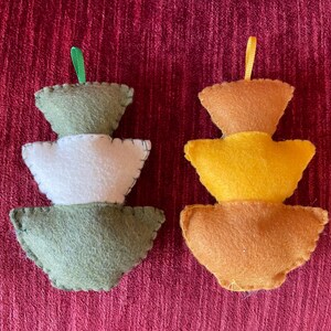 K&ouml;nnte beinhalten: Zwei Weihnachtsbaumschmuck aus Filz, einer gr&uuml;n und wei&szlig;, der andere orange und gelb. Beide haben eine Schlaufe zum Aufh&auml;ngen.