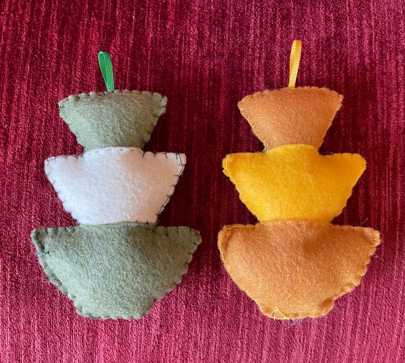 K&ouml;nnte beinhalten: Zwei Weihnachtsbaumschmuck aus Filz, einer gr&uuml;n und wei&szlig;, der andere orange und gelb. Beide haben eine Schlaufe zum Aufh&auml;ngen.