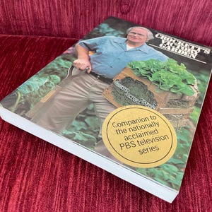 May include: A softcover book titled Crockett's Victory Garden featuring a photograph of a person in a blue shirt and tan pants holding a wooden crate of lettuce. A round gold sticker on the cover reads Companion to the nationally acclaimed PBS television series.