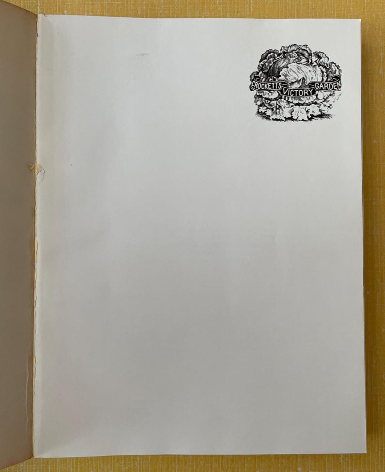 May include: A white page from a book featuring a black and white ink illustration of a head of lettuce in the upper right corner. A banner draped across the lettuce contains the text Crockett's Victory Garden in a clear, legible font.