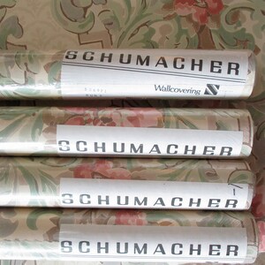 May include: Four rolls of Schumacher wallpaper featuring a floral and leaf design in pink, green, and beige. Each roll is labelled with the Schumacher logo and the words "Wallcovering".