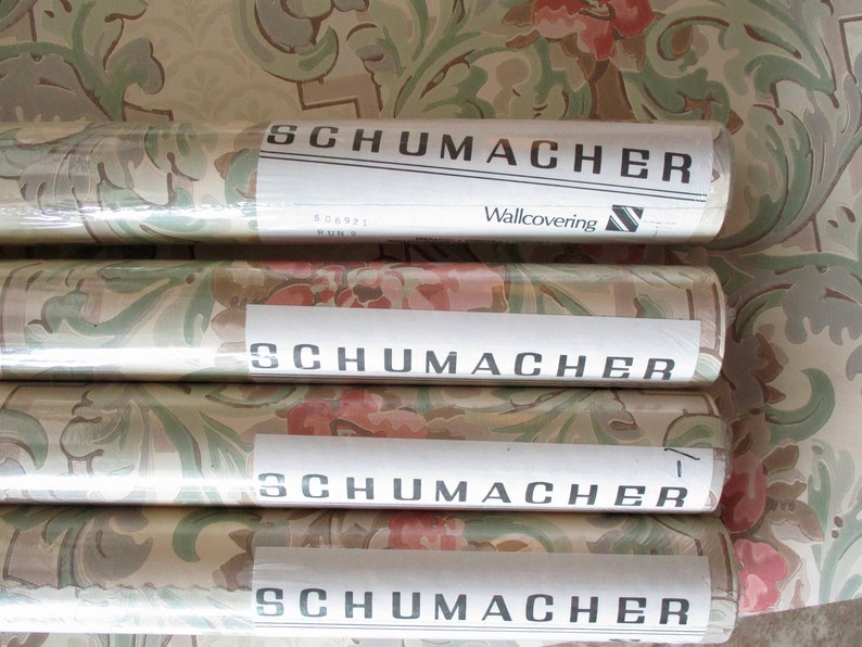 May include: Four rolls of Schumacher wallpaper featuring a floral and leaf design in pink, green, and beige. Each roll is labelled with the Schumacher logo and the words "Wallcovering".