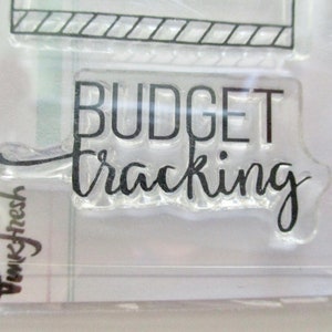 May include: Clear acrylic stamp with the words "BUDGET tracking" in black, handwritten-style font. The stamp is part of a set, with a partial view of another stamp at the top. The brand name "Pinkfresh" is visible in the lower left corner.