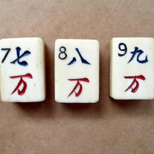 May include: Three off-white rectangular mahjong tiles featuring the numbers 7, 8, and 9 in black ink. Each tile displays a blue Chinese character for the number and a red Chinese character for ten thousand, all deeply engraved into the surface.
