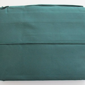 May include: Folded, solid-colored, teal-green bed sheet set. The top edge is folded over, and a horizontal seam runs across the middle. The fabric appears to be a smooth, woven material. The sheets are neatly folded.