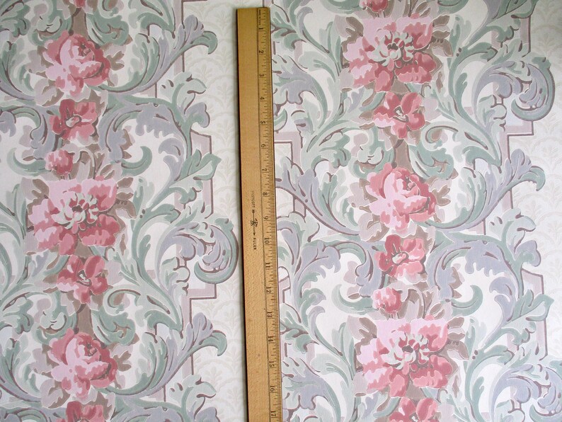 May include: Vintage wallpaper with a repeating floral pattern. The design features large pink roses, gray and green foliage, and a white background. A wooden ruler, approximately 30 cm long, is placed vertically on the wallpaper.