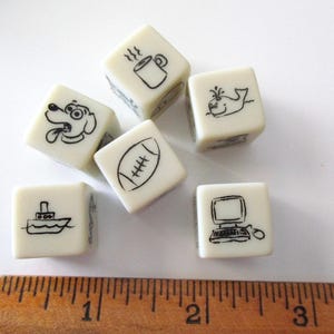 May include: Six ivory-colored dice with black line drawings of a dog, coffee mug, whale, football, boat, and computer. A wooden ruler with inch markings is at the bottom of the image.