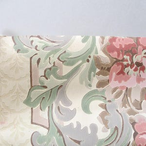May include: A fragment of vintage wallpaper with a floral and scroll design. The pattern features large pink and brown flowers, green leaves, and grey scrollwork on a cream background. The edge of the paper is torn.