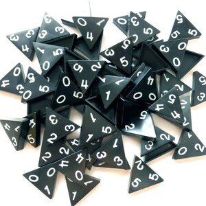 May include: A collection of black triangular game pieces with white numbers from 0 to 5. The pieces are scattered on a white surface, with some overlapping. The numbers are clearly visible on each piece.