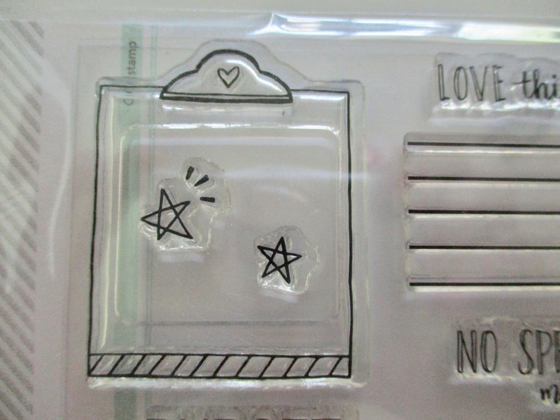 May include: Clear stamp set featuring a clipboard design with a heart and two star shapes. The set includes the text "LOVE this" and other text. Ideal for scrapbooking and crafting projects.