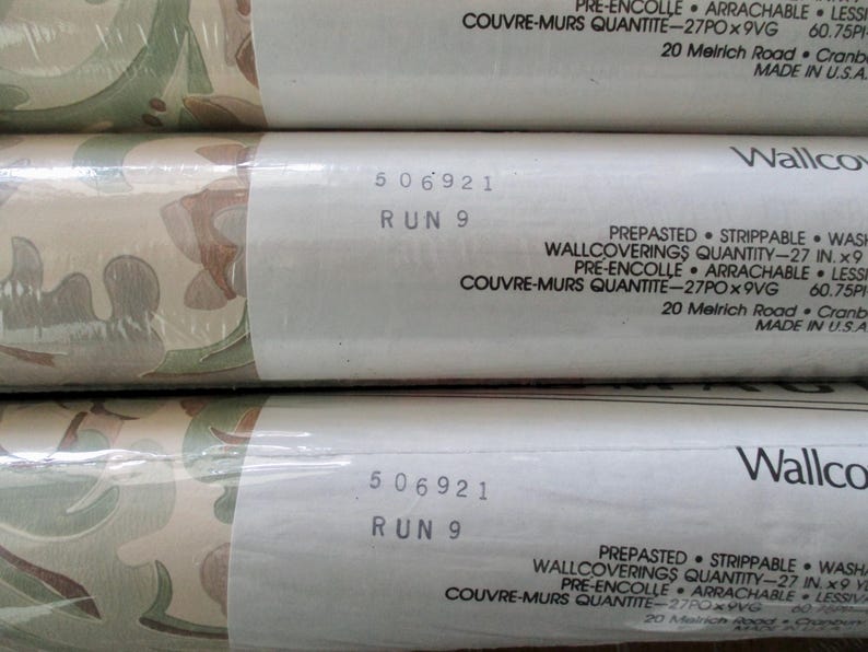 May include: Three rolls of pre-pasted, strippable wallpaper. The wallpaper features a repeating pattern of green, brown, and beige organic shapes. The label reads "WALLCOVERINGS QUANTITY - 27 IN. x 9". The text "506921 RUN 9" is also visible.