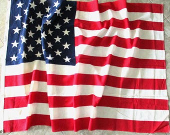 May include: A United States flag with a blue canton filled with white stars and alternating red and white stripes. The flag is made of fabric and appears to be waving slightly.