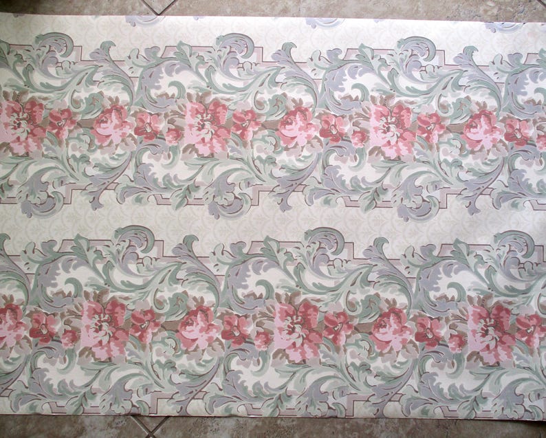 May include: Wallpaper with a repeating floral pattern. The design features rows of pink roses and grey, green, and white scrollwork on a cream background. The wallpaper has a vintage aesthetic.