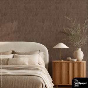 May include: A bedroom scene featuring a curved cream-colored headboard with layered beige bedding, a light wood fluted nightstand, a white table lamp, and a ceramic vase with dried branches against brown wallpaper with a subtle diamond pattern.