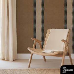 May include: A light wood armchair with a woven seat and back, draped with a cream-colored blanket. The chair sits in front of a brown and beige striped wallpaper. A cream-colored curtain is on the left.
