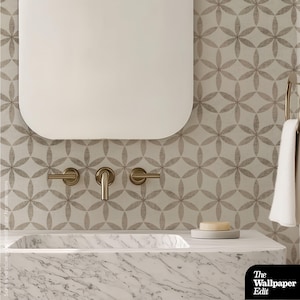 May include: A modern bathroom vanity with a marble countertop and a built-in sink. The vanity features a large, rounded-corner mirror and brushed gold fixtures. The wall is decorated with a floral pattern wallpaper in shades of gray and white. A bar of soap rests on a small gray soap dish.