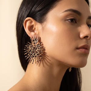Peut inclure: Une grande boucle d'oreille circulaire en forme d'étoile avec des pointes rayonnantes. La surface de la boucle d'oreille est recouverte d'un motif léopard marron et noir, créant une apparence texturée audacieuse qui s'étend depuis le centre.