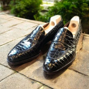 May include: A pair of black leather loafers with a crocodile pattern. The loafers have a pointed toe and a slip-on design.