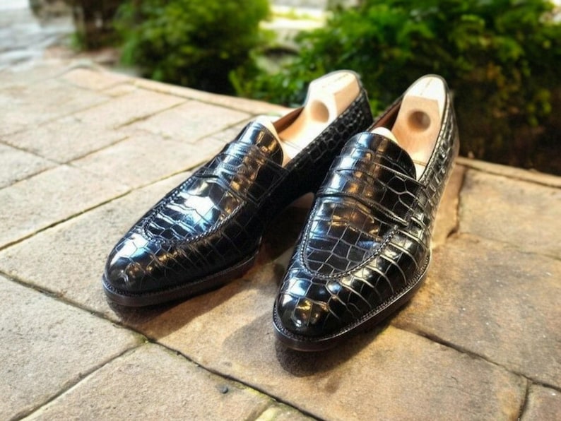 May include: A pair of black leather loafers with a crocodile pattern. The loafers have a pointed toe and a slip-on design.