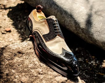 May include: A black and white leather Oxford shoe with brogue detailing. The shoe has a black leather toe cap and a white leather upper. The shoe is laced with black laces.