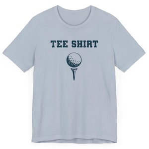 May include: A light blue t-shirt with the text "TEE SHIRT" in dark blue letters and a golf ball on a tee printed in dark blue.