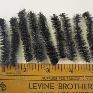 May include: Black pipe cleaners, approximately 5 inches long, arranged in a row on a wooden ruler. The ruler is marked with inches and has the text "Falcon" and "Made in U.S.A."