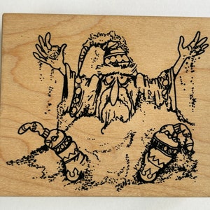 May include: A wooden stamp featuring a whimsical illustration of a wizard with outstretched arms, seemingly conjuring something. The wizard is depicted with a long beard, hat, and ornate sleeves. The stamp is perfect for crafting and scrapbooking projects.