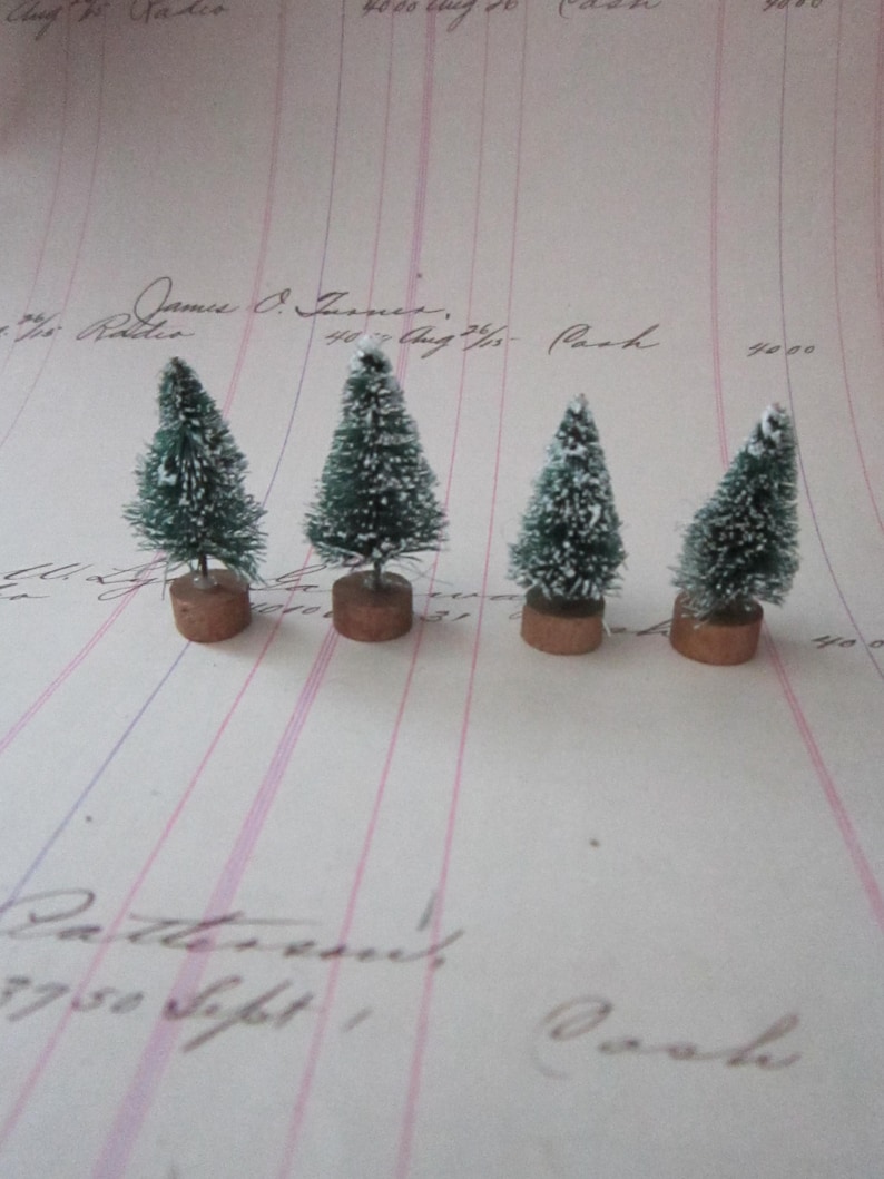 Peut inclure: Quatre petits sapins artificiels enneig&eacute;s sur un fond blanc avec des lignes roses et bleues. Les sapins sont verts avec un flocage blanc et sont sur des bases brunes.