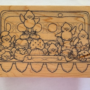 May include: A wooden stamp featuring an egg carton filled with decorated Easter eggs and cartoon chicks. The chicks are in various poses, some wearing shoes and others emerging from the eggs. The design is outlined in black.