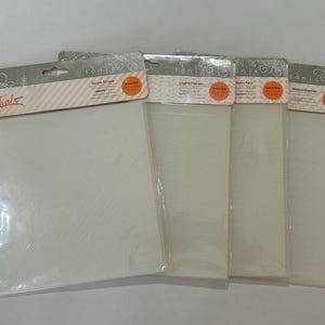 May include: Four Tonic Studios Essentials embossing folders in clear plastic packaging. Each folder is white with a distinct texture, including Simple Stripes, Layered Leaves, Retro Face, and Modern Diamonds, labeled with orange circular stickers.