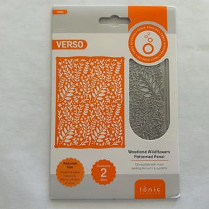 May include: A packaging for a set of two metal dies for crafting. The dies feature a woodland wildflowers patterned design. The packaging is white with orange text and a small image of the dies. The text on the packaging reads "Woodland Wildflowers Patterned Panel" and "Contains 2 dies".
