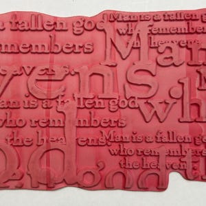 May include: A red rubber stamp with the text "Man is a fallen god who remembers the heavens." The stamp has a unique, irregular shape and features raised lettering for imprinting.