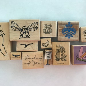 May include: A collection of 11 wooden rubber stamps with various designs, including a ladybug, a birdhouse, a dragonfly, a flower pot, a speed limit sign, and the words "Thinking of You".