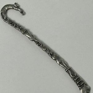 May include: Silver bookmark with a cat design. The bookmark is shaped like a cat's tail and has a cat's head at the top. The cat is curled up and has a small bell on its collar.