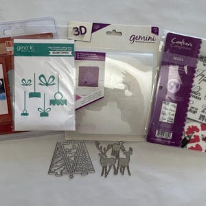 May include: A collection of crafting supplies including a Gina K. Designs holiday topper die set, a Gemini 3D embossing folder, and a Crafter's Companion Noel stamp set. Loose metal dies shaped like two Christmas trees and two reindeer are included.