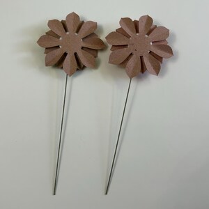 May include: Two brown paper flowers on wire stems. The flowers have a circular center and eight petals.