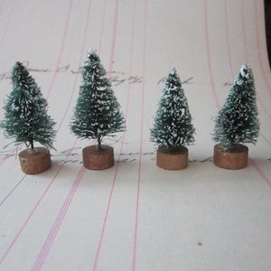 Peut inclure: Quatre mini sapins de No&euml;l artificiels avec de la neige floqu&eacute;e blanche sur des branches vertes. Les sapins sont sur de petites bases brunes.