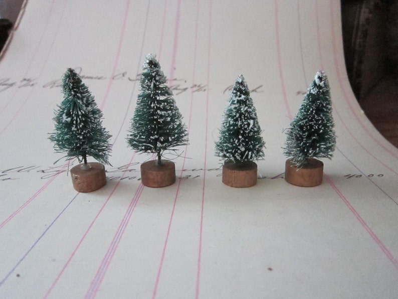 Peut inclure: Quatre mini sapins de No&euml;l artificiels avec de la neige floqu&eacute;e blanche sur des branches vertes. Les sapins sont sur de petites bases brunes.