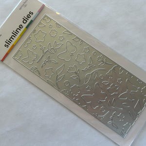 May include: A silver-colored slimline die set featuring a floral and butterfly design. The die set includes various flower and leaf shapes, along with butterfly outlines. The packaging includes the text "slimline dies" and "spring floral".